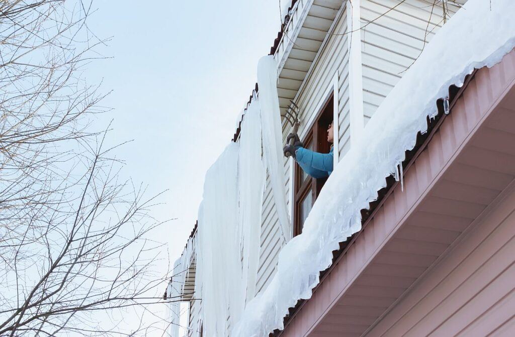 A man removes giant icicles and snow from the roof