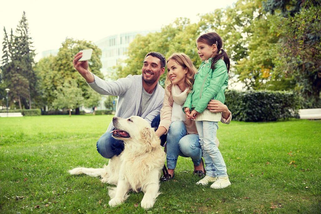 快樂的家庭與拉布拉多獵犬在公園裡用智慧手機自拍