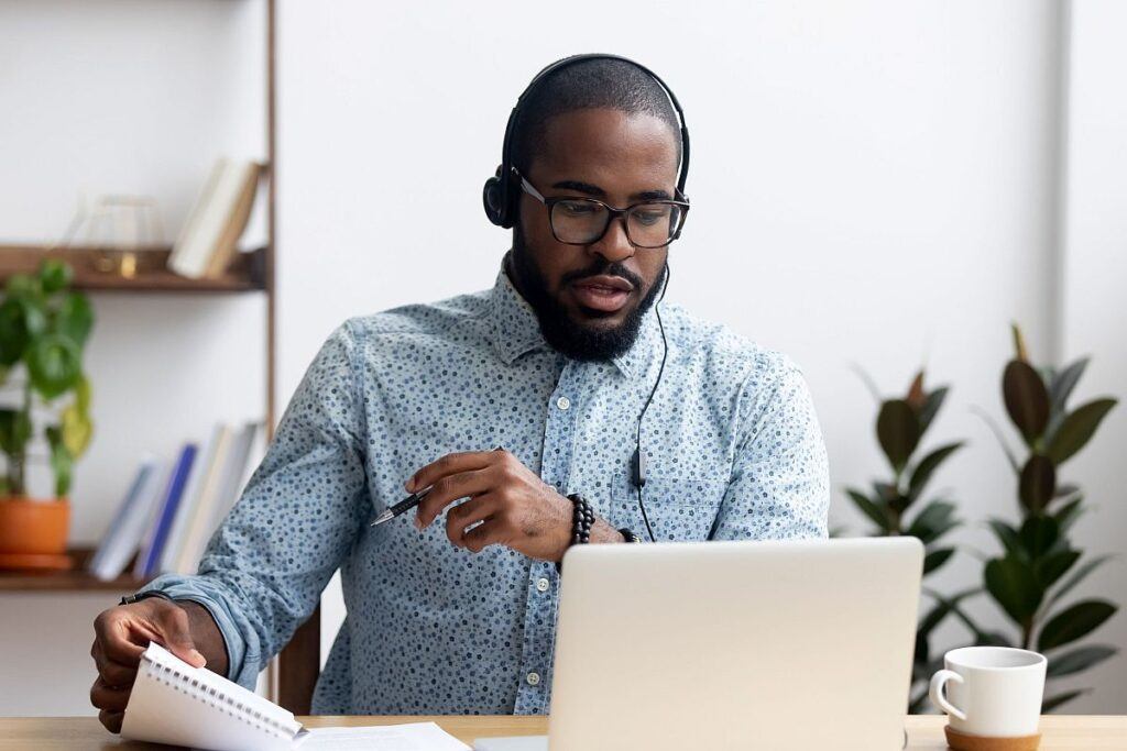 Black young man sitting at table wearing headphones learn foreign language