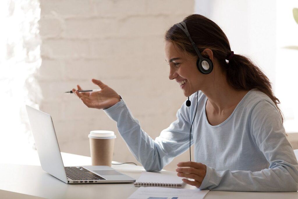 smiling lady freelancer wearing headset, communicating with client via video computer call
